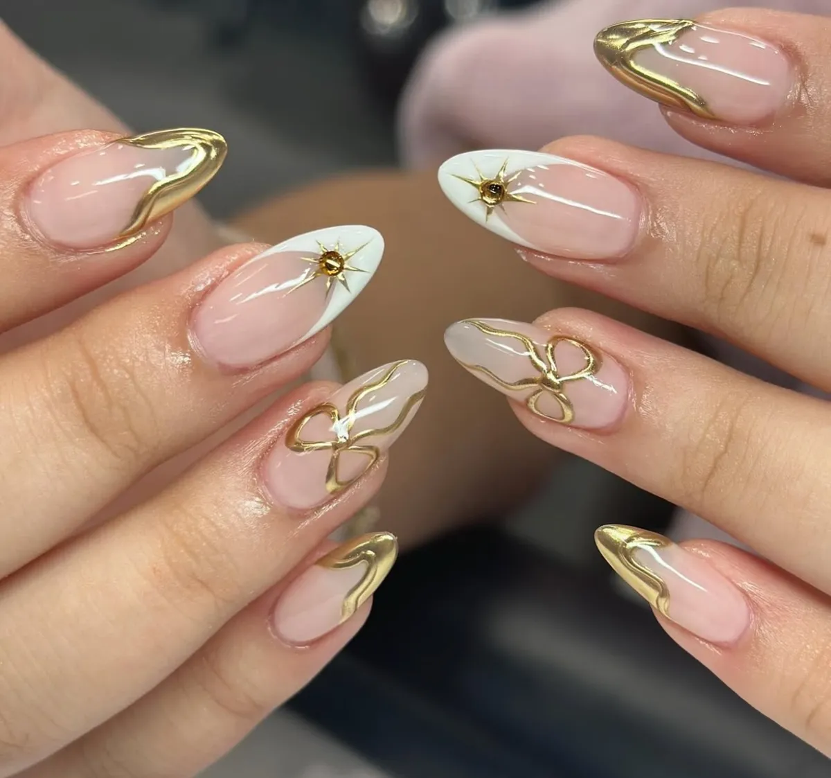 Gold-edged nude nails with white tips, starbursts, and bow linework