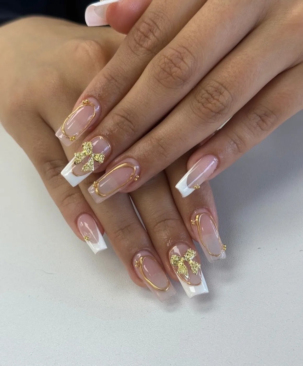 White French tips with raised gold frames and bow charms