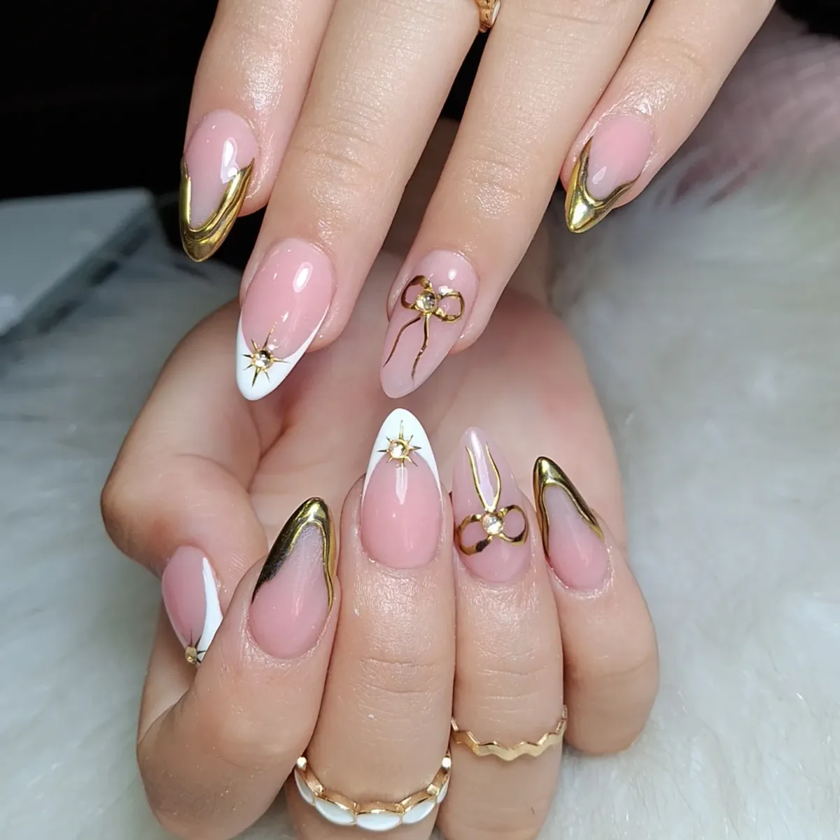 Gold V-tips and bow accents on pink nails