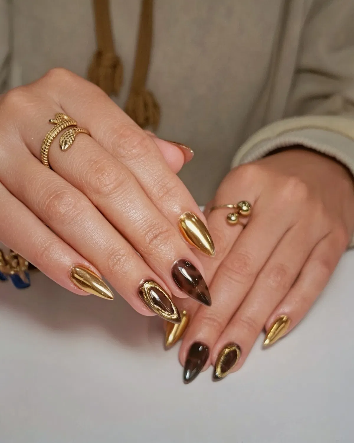 Gold chrome nails paired with dark brown and gold-framed accents