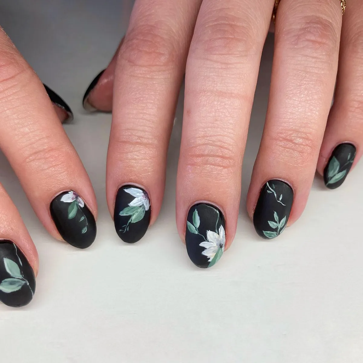 Black nails with white flowers and green leaves