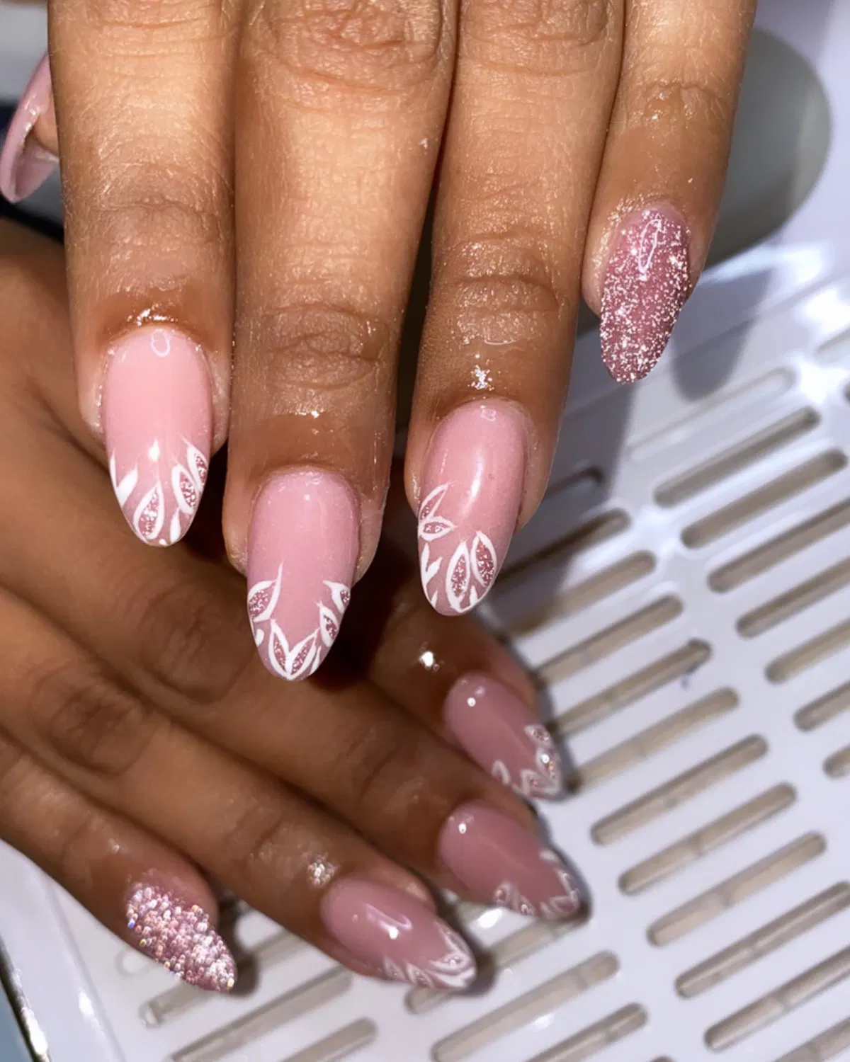 Soft pink almond nails with white leafy tips and glitter accents
