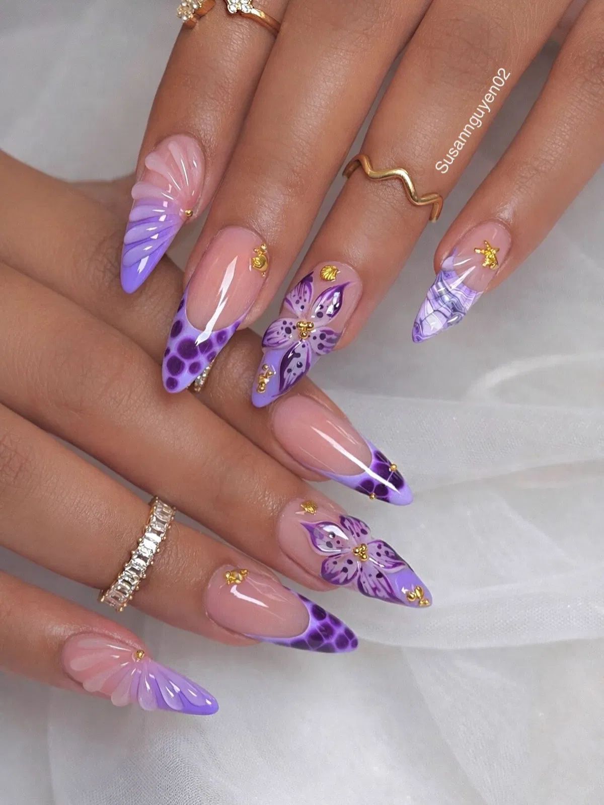 Nude base with purple tips, floral motifs, and small gold charms