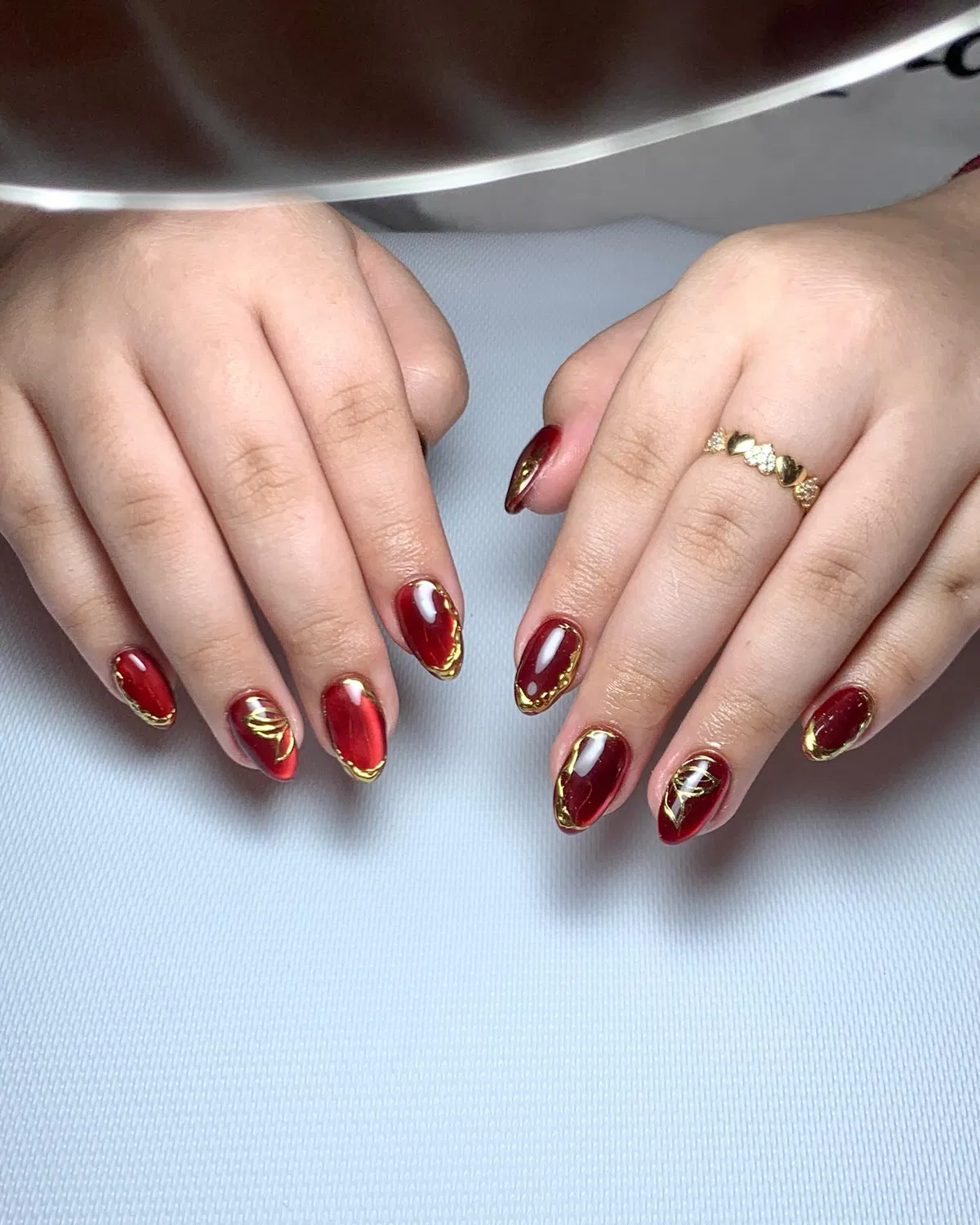 Deep red glossy nails with gold outline edging and swirl accents