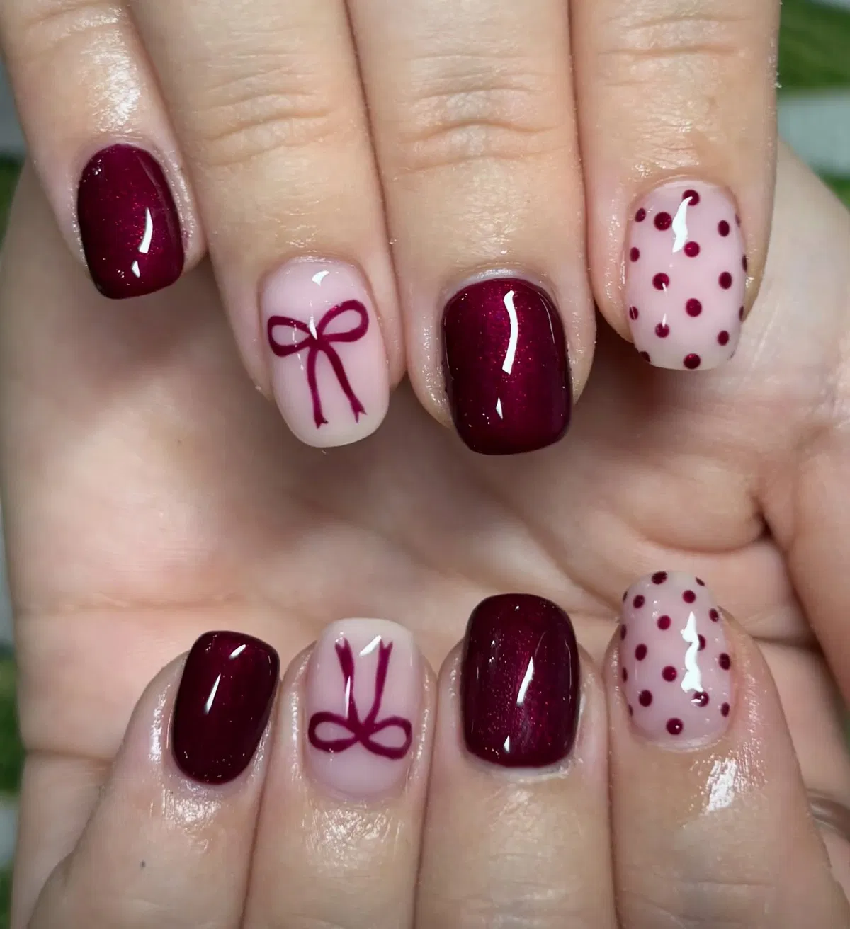 Burgundy sparkle nails with nude bow and polka-dot accents