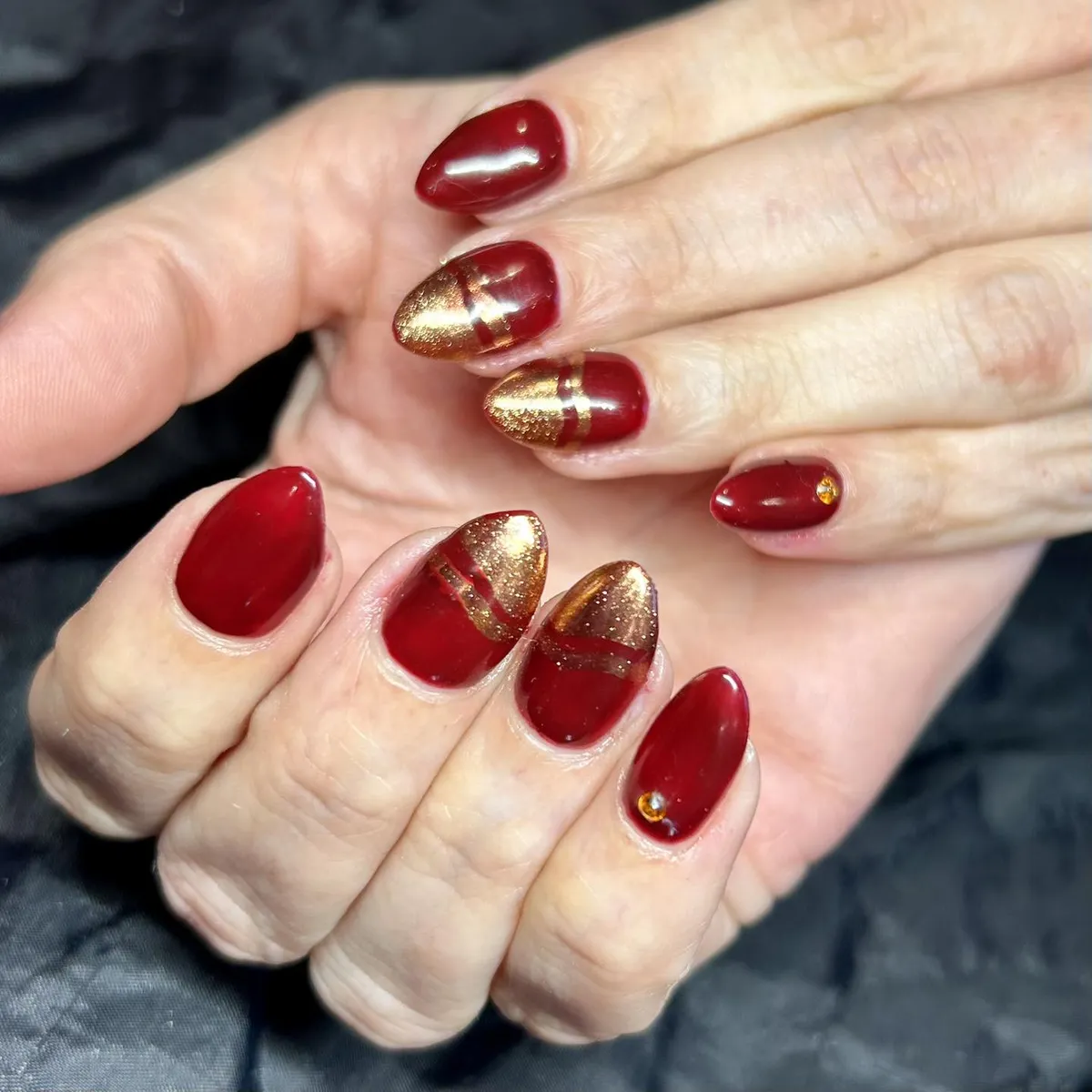Deep red nails with gold glitter blocks and small gems