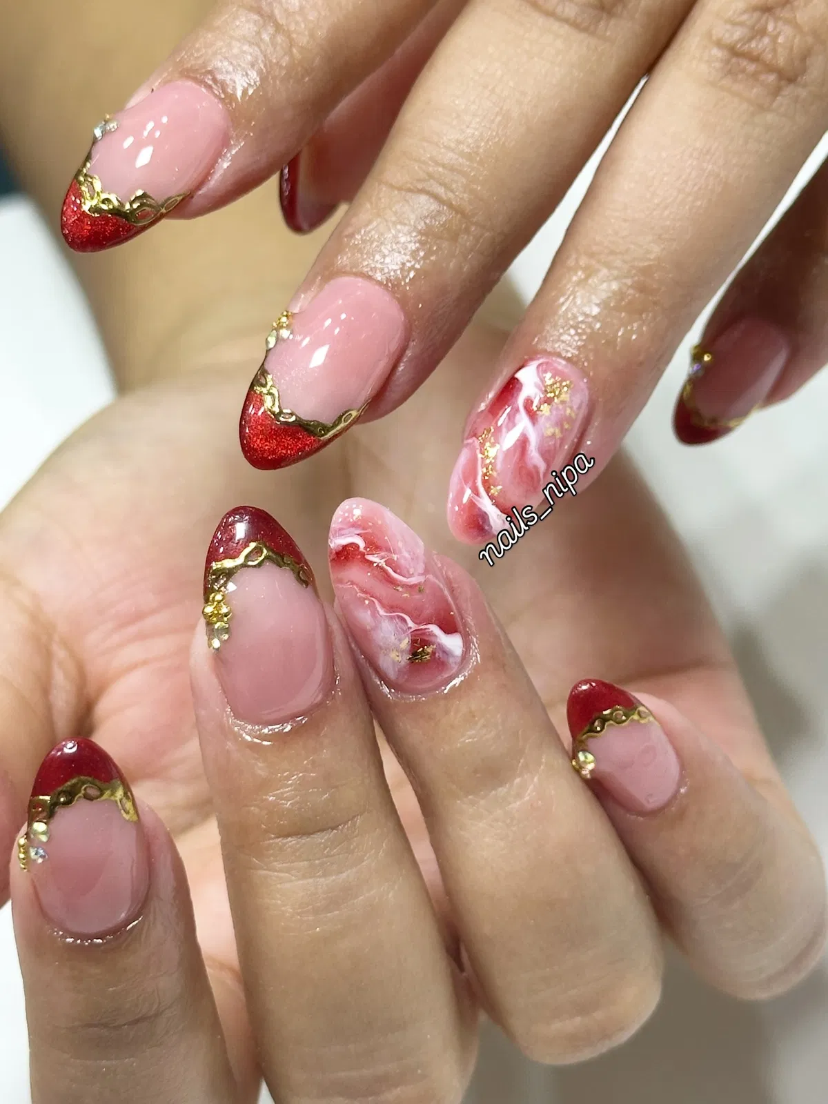Red glitter French tips with gold edging and marbled accent nail