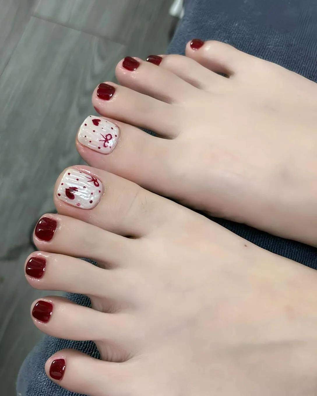 Deep red pedicure with heart-themed white accent big toes