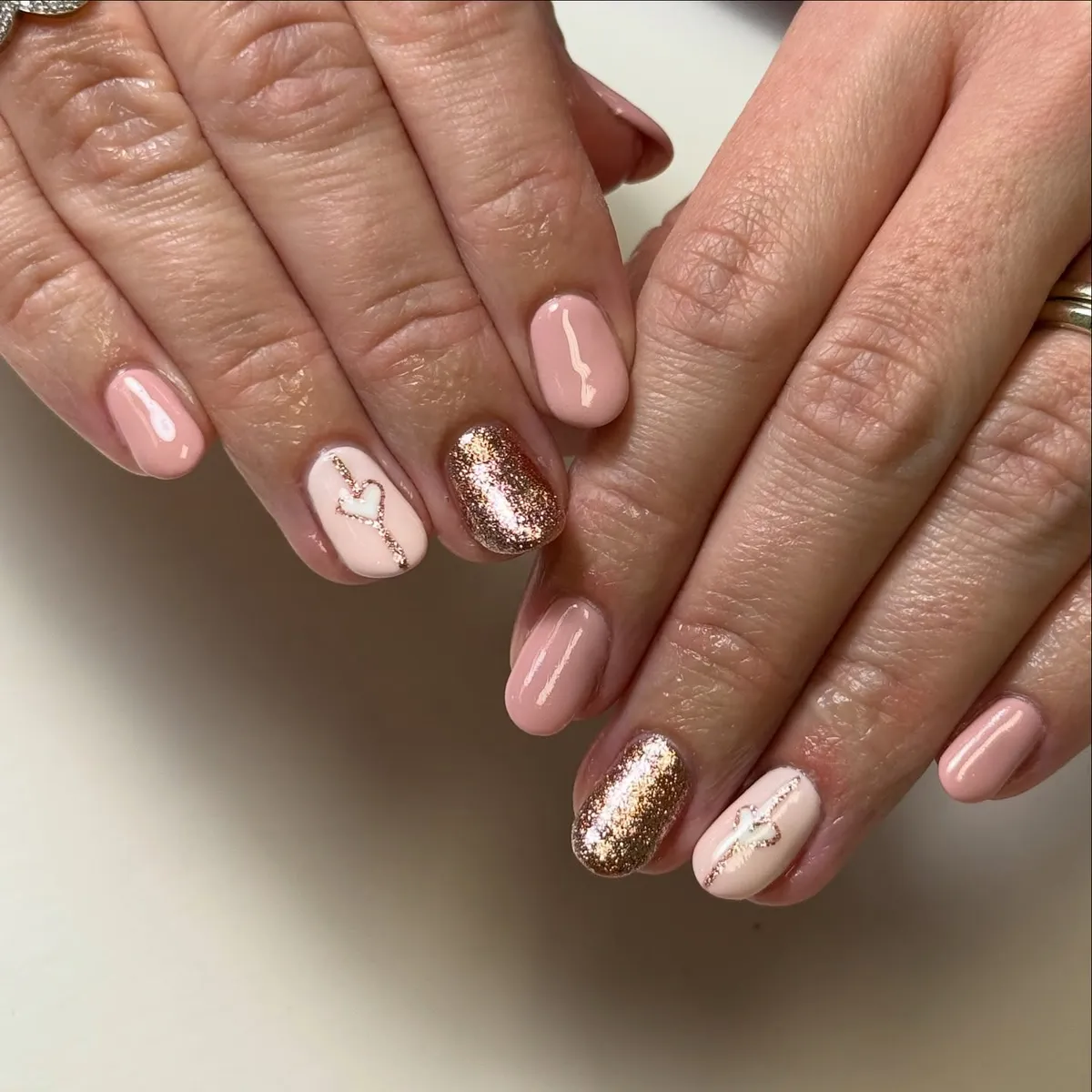 Short pale pink nails with rose-gold glitter accents and heart details