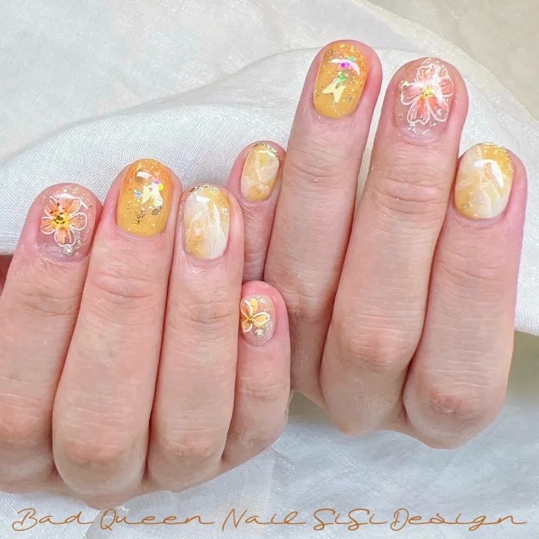 Yellow-orange translucent nails with glitter and white floral outlines