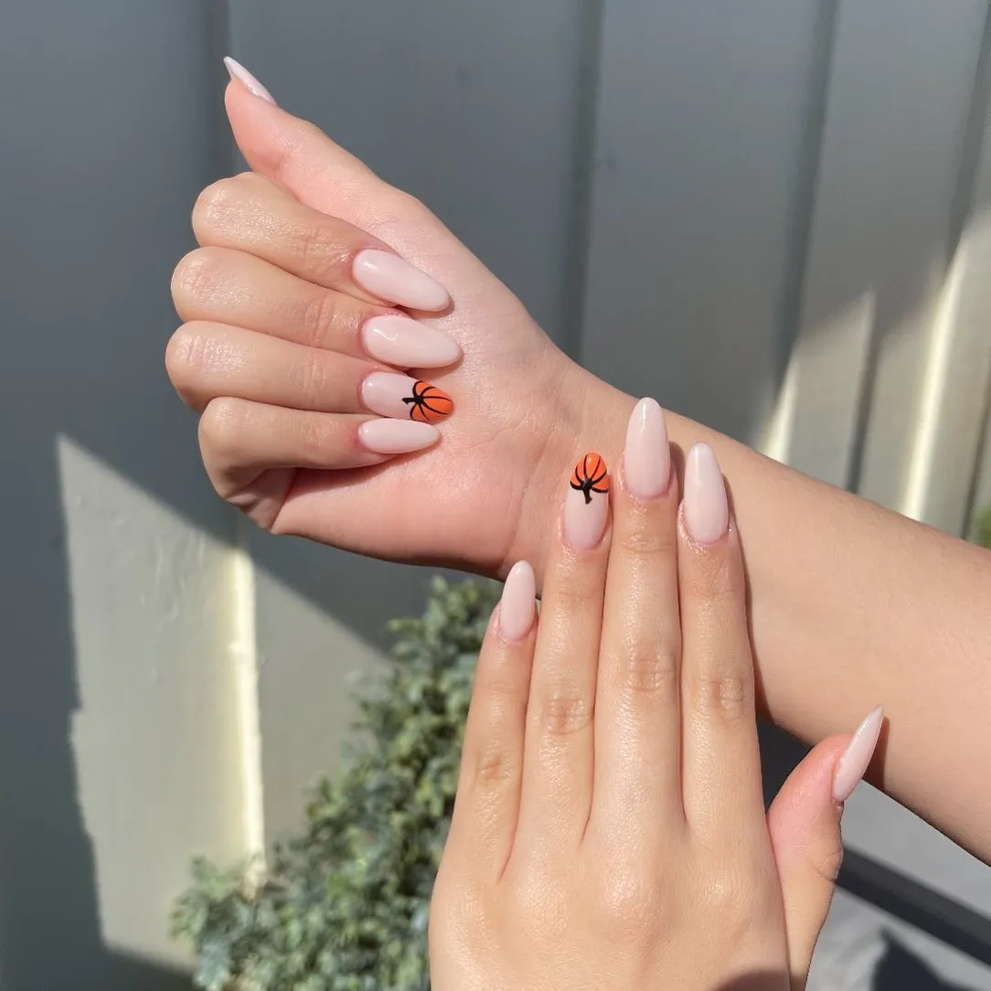 Nude-pink almond nails with small pumpkin accents