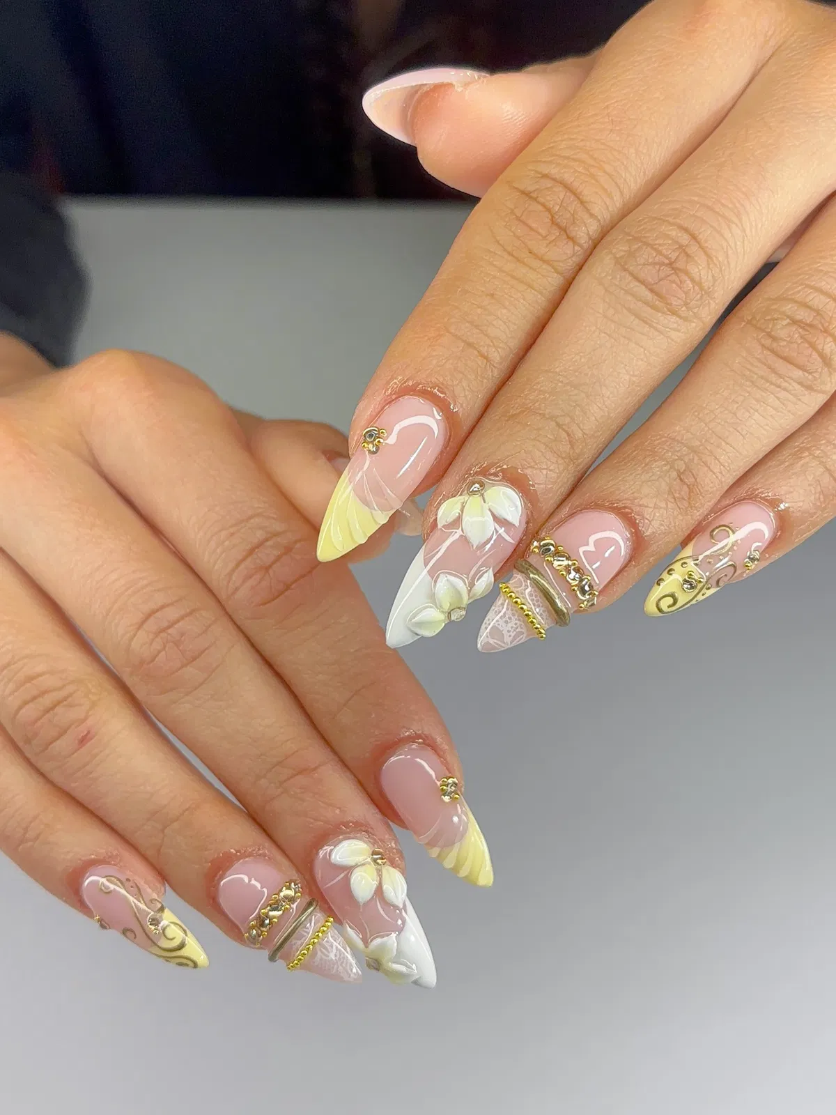 Nude stiletto nails with yellow/white tips, raised flowers, and gold detailing