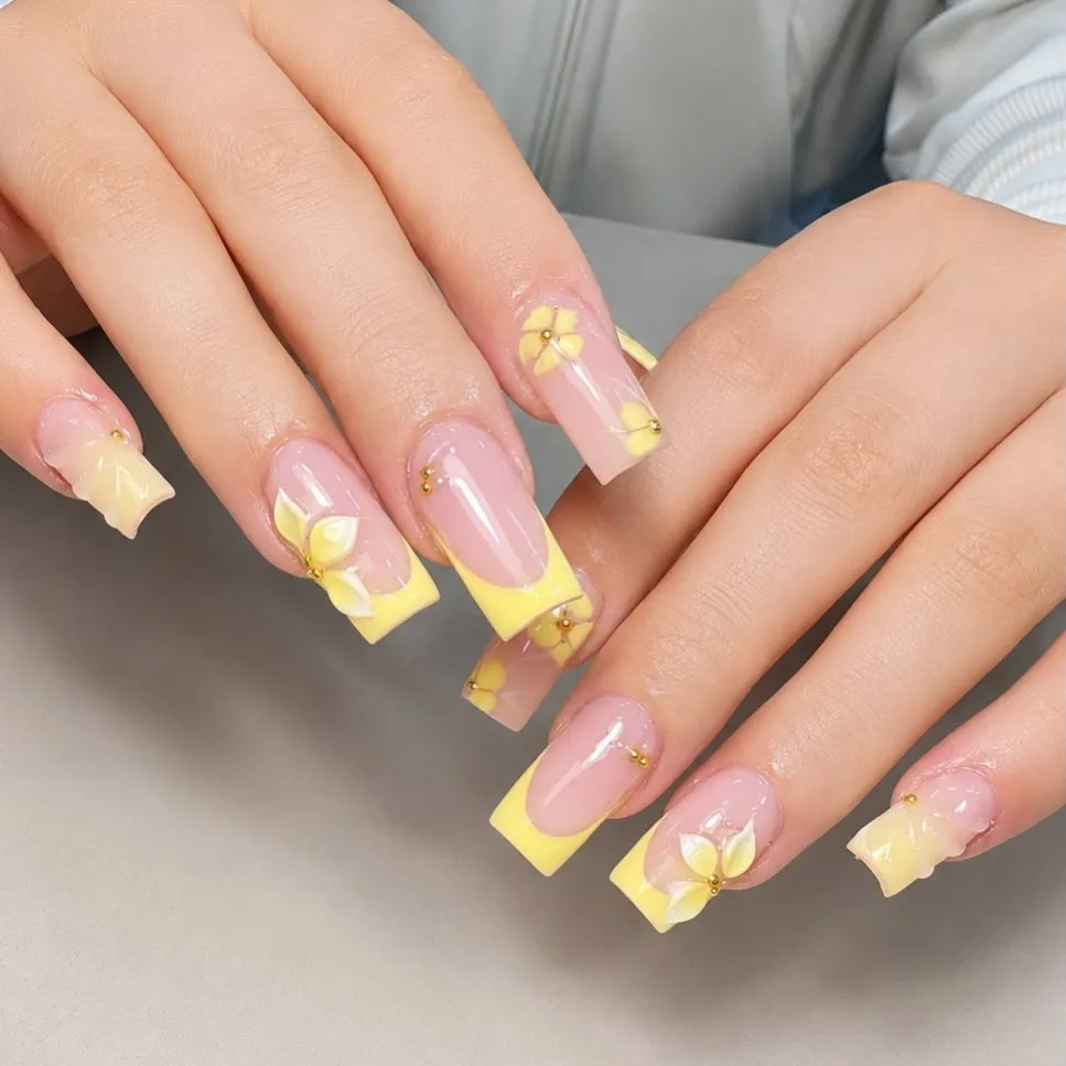Pale yellow French tips with small floral details and gold beads