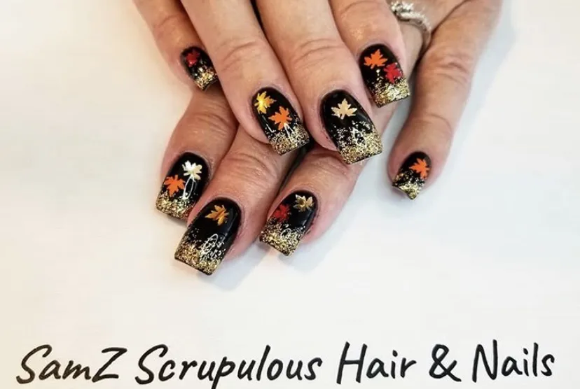 Black nails with gold glitter tips and leaf decals