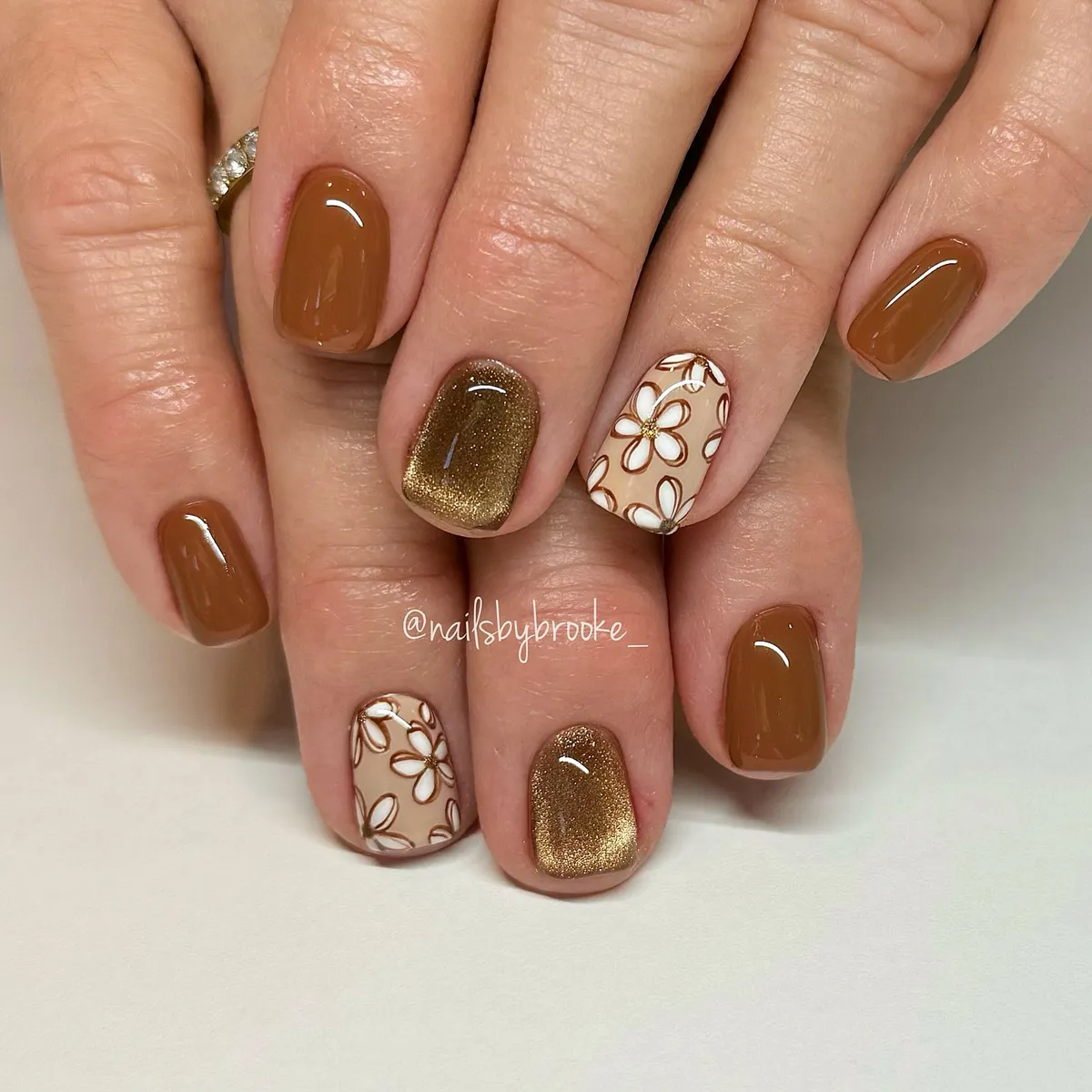 Glossy brown nails with gold glitter and outlined florals