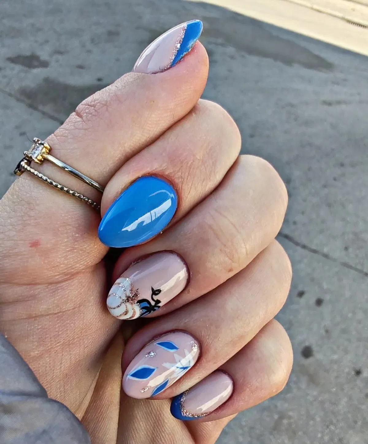 Bright blue statement nail with nude-and-blue French tips and leaf accents