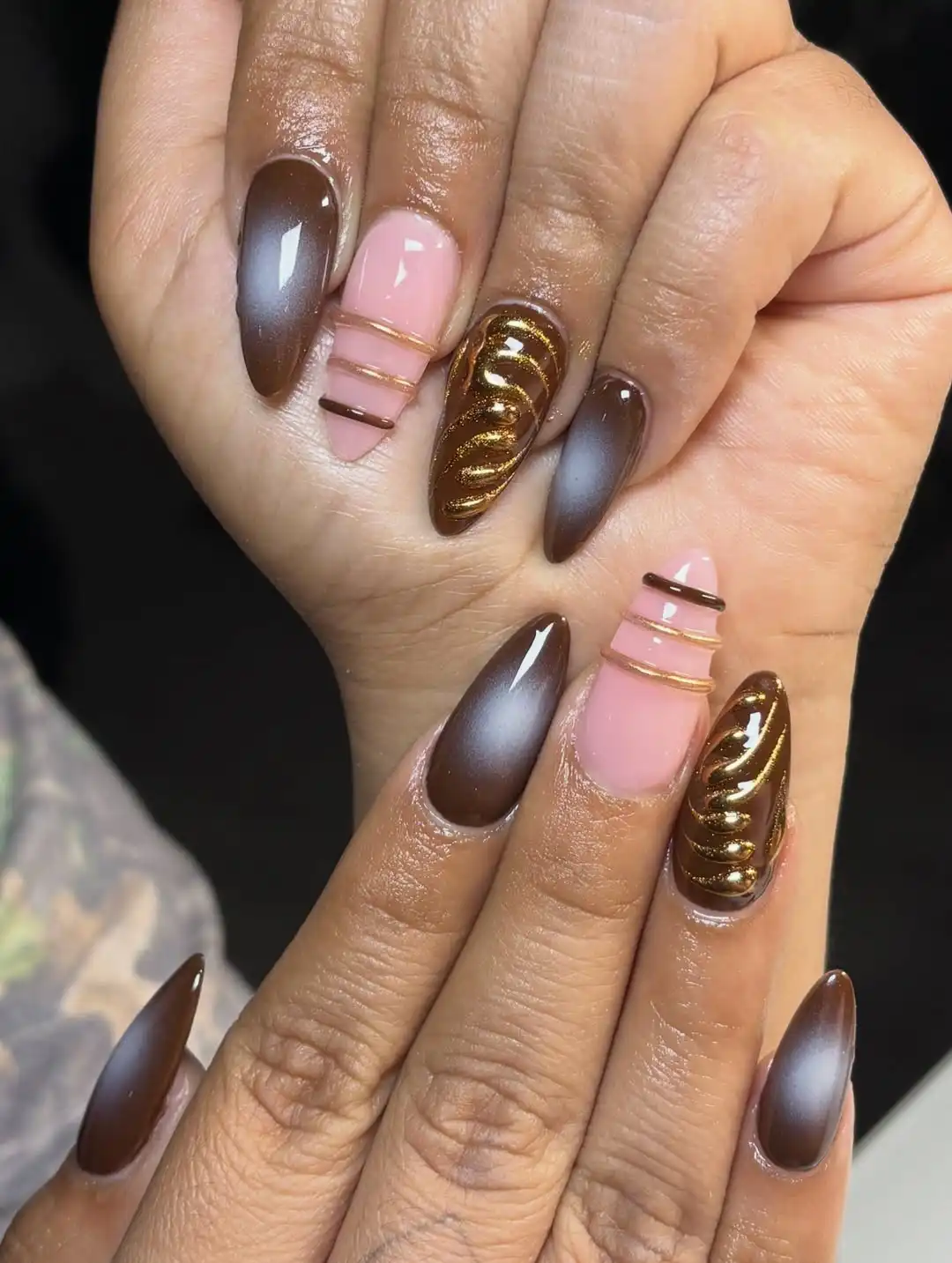 Brown reflective nails with pink-and-gold striping and raised gold accent