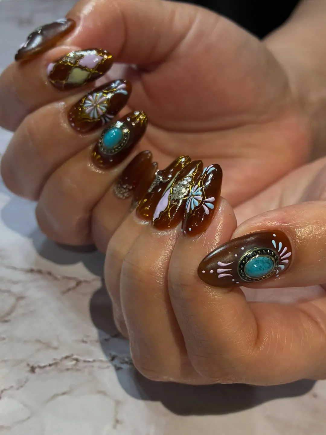 Glossy brown almond nails with turquoise stones and gold detailing