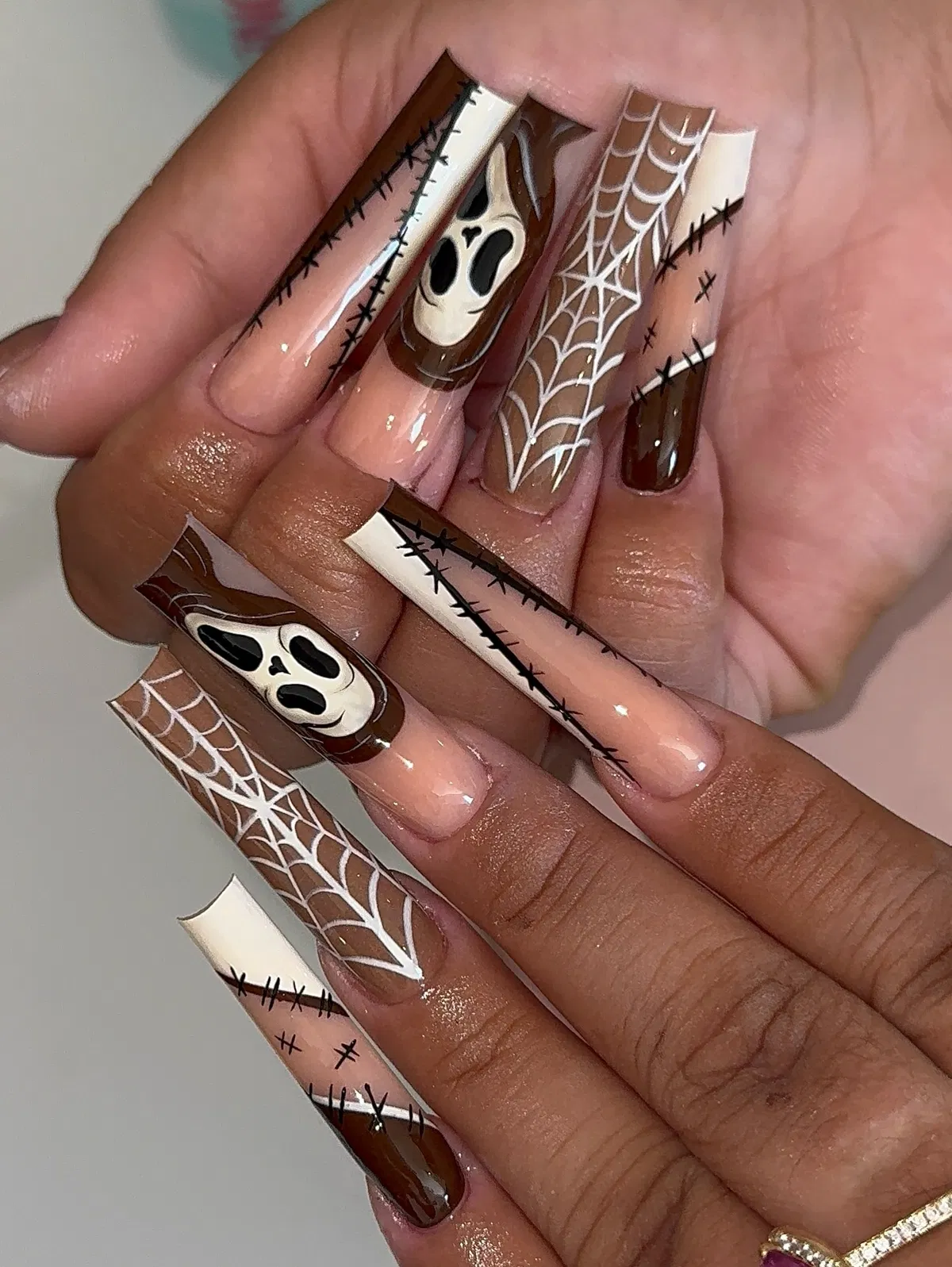 Brown-and-nude graphic nails with spiderwebs and ghost-face art