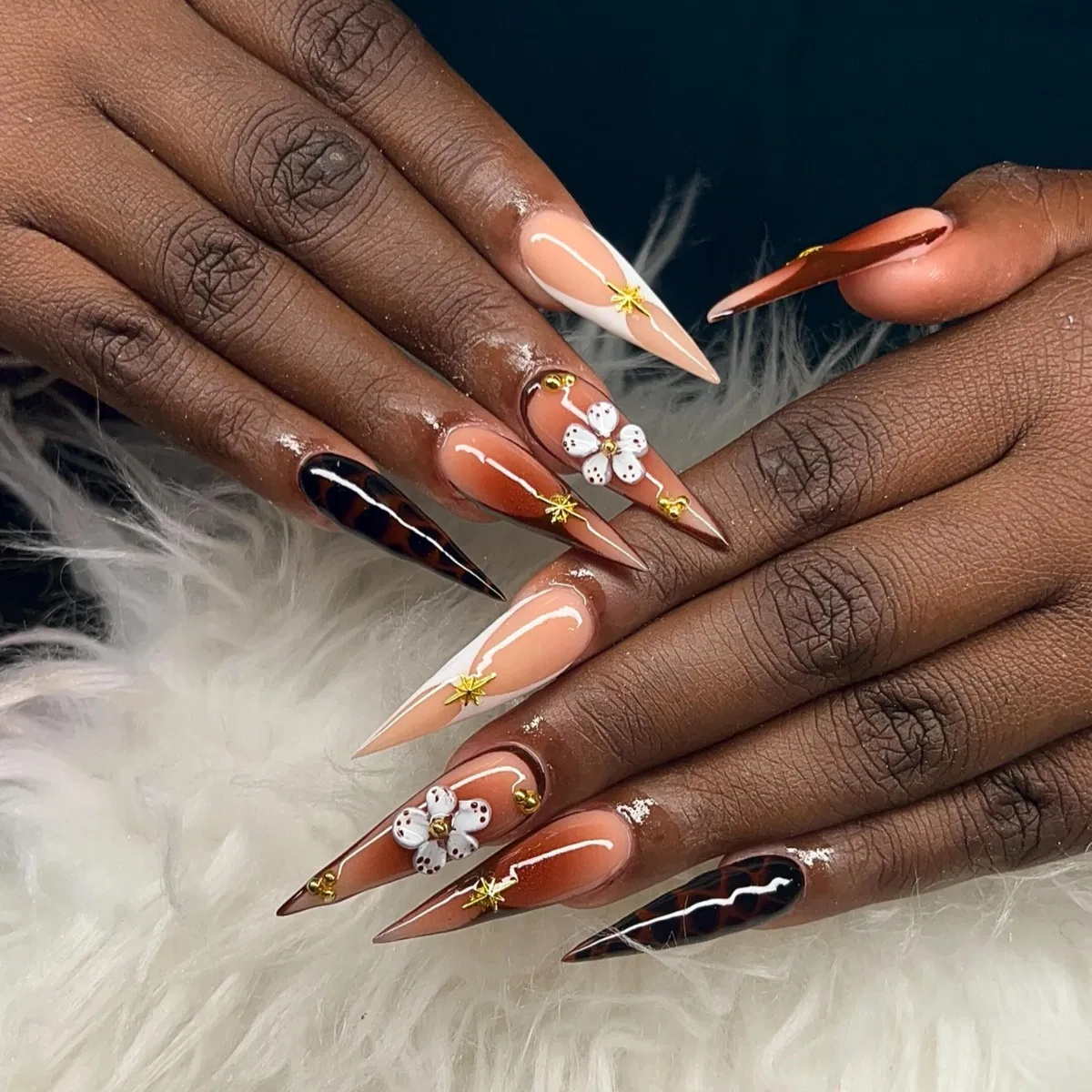 Long stiletto nude-and-brown tips with gold stars and 3D flowers