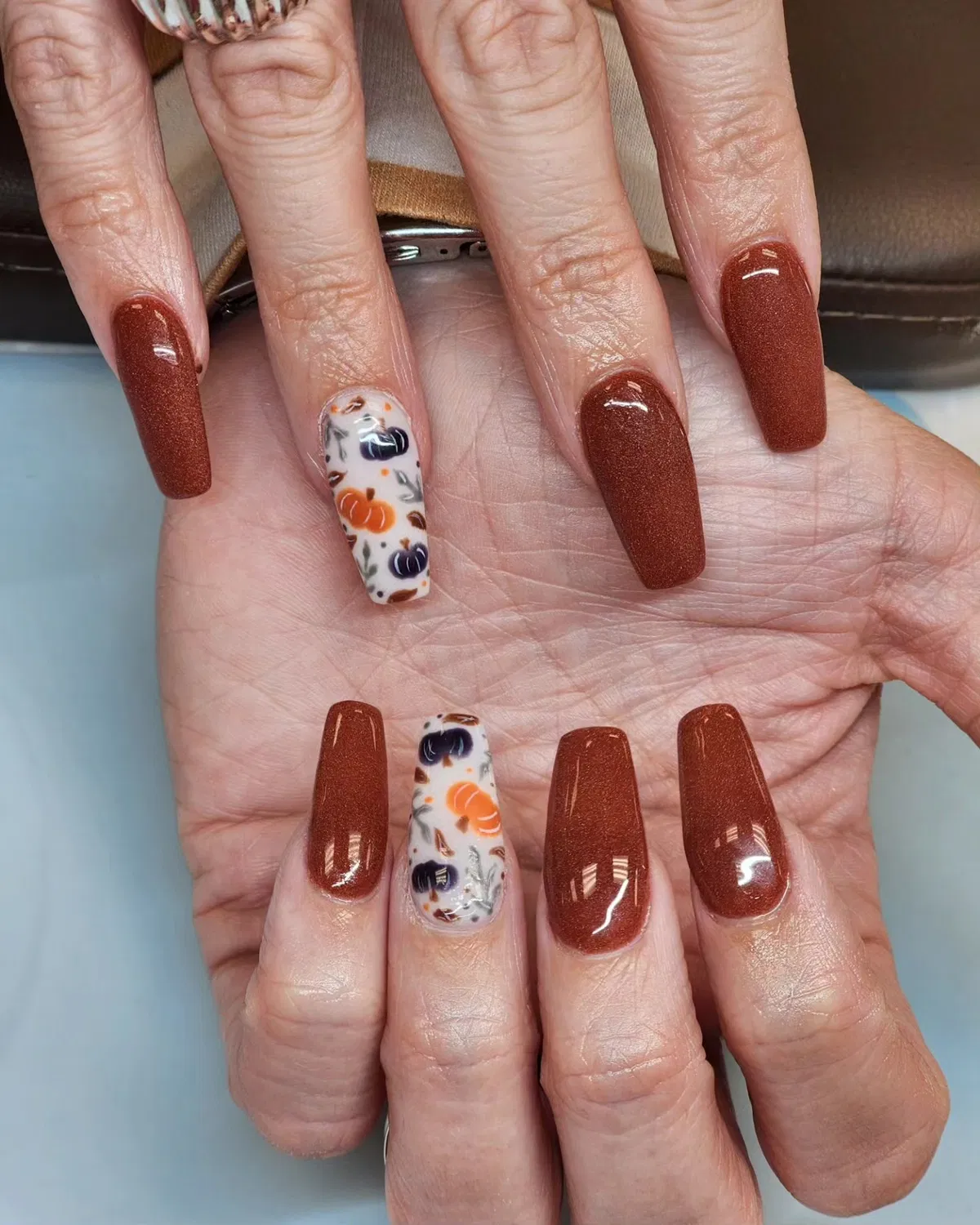 Shimmery brown coffin nails with pumpkin-print accents