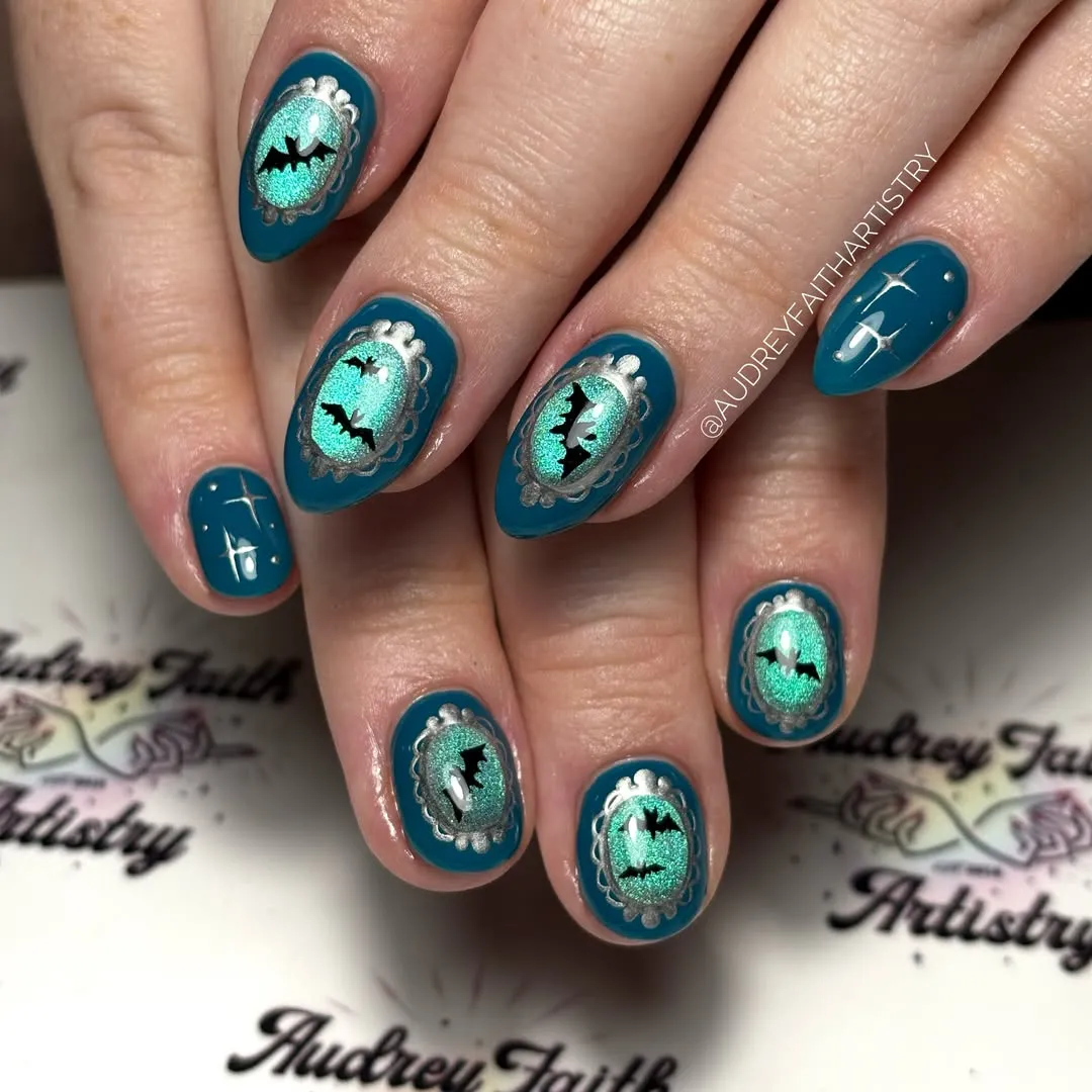 Teal cameo-style nails with bat silhouettes and silver frames