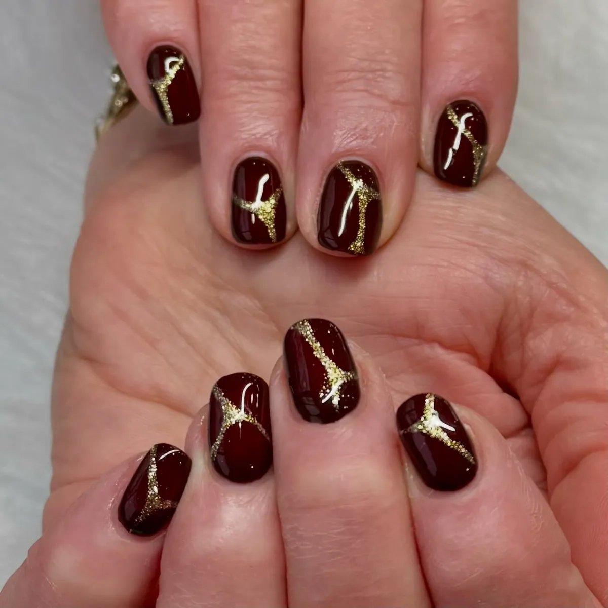 Deep burgundy nails with gold glitter linework