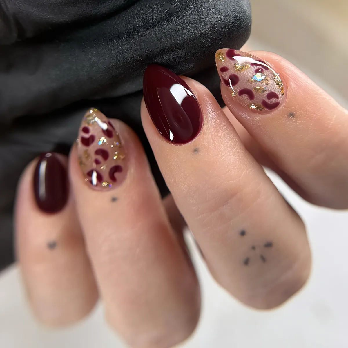 Burgundy nails with gold foil-like accents and curved spot pattern