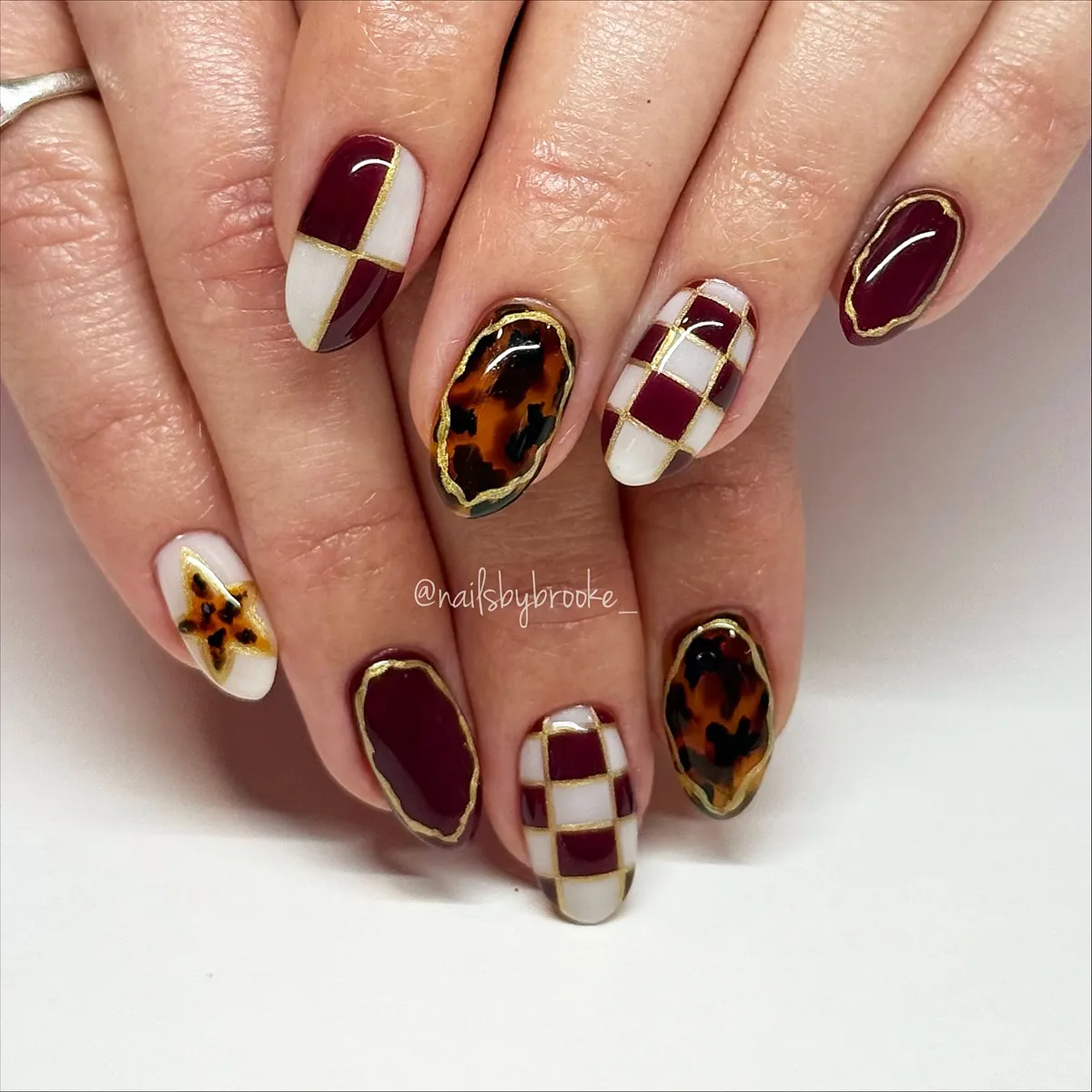 Burgundy-and-white geometric nails with gold lines and mottled accents