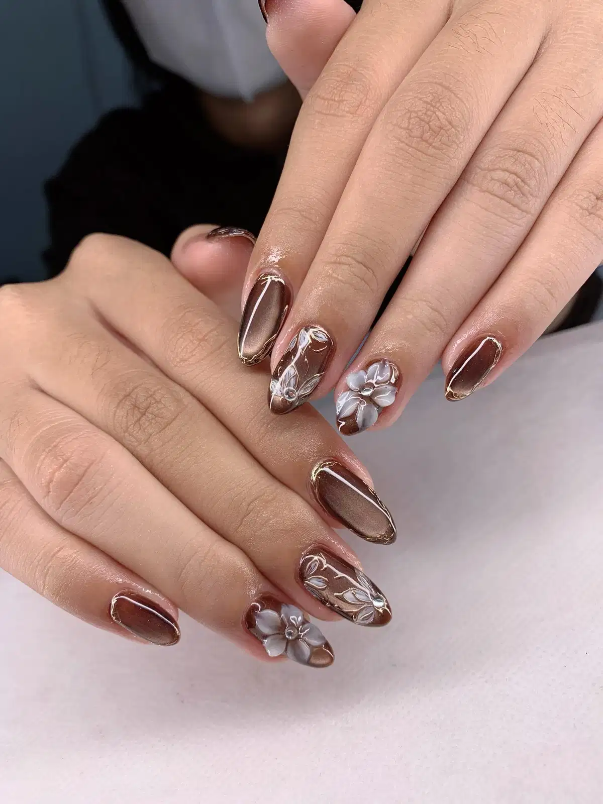 Long brown nails with gold outlines and raised white floral accents