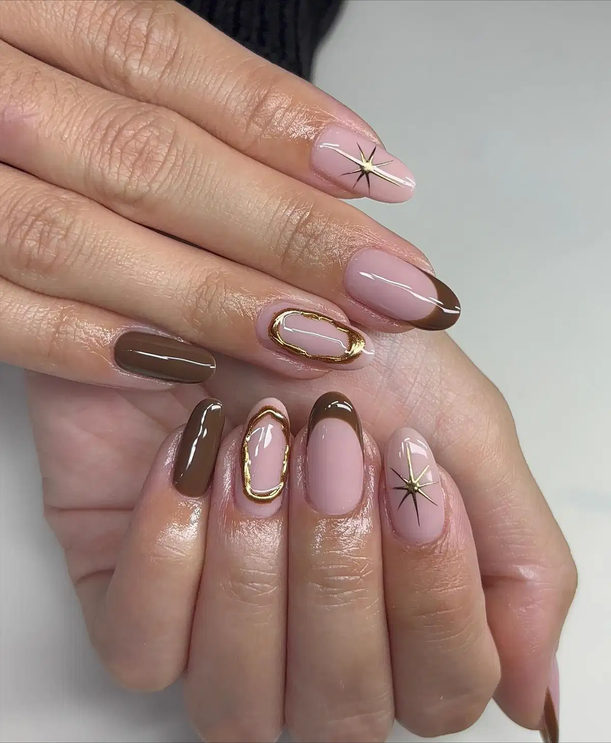 Nude-pink and brown French tips with gold starburst and oval frame accents