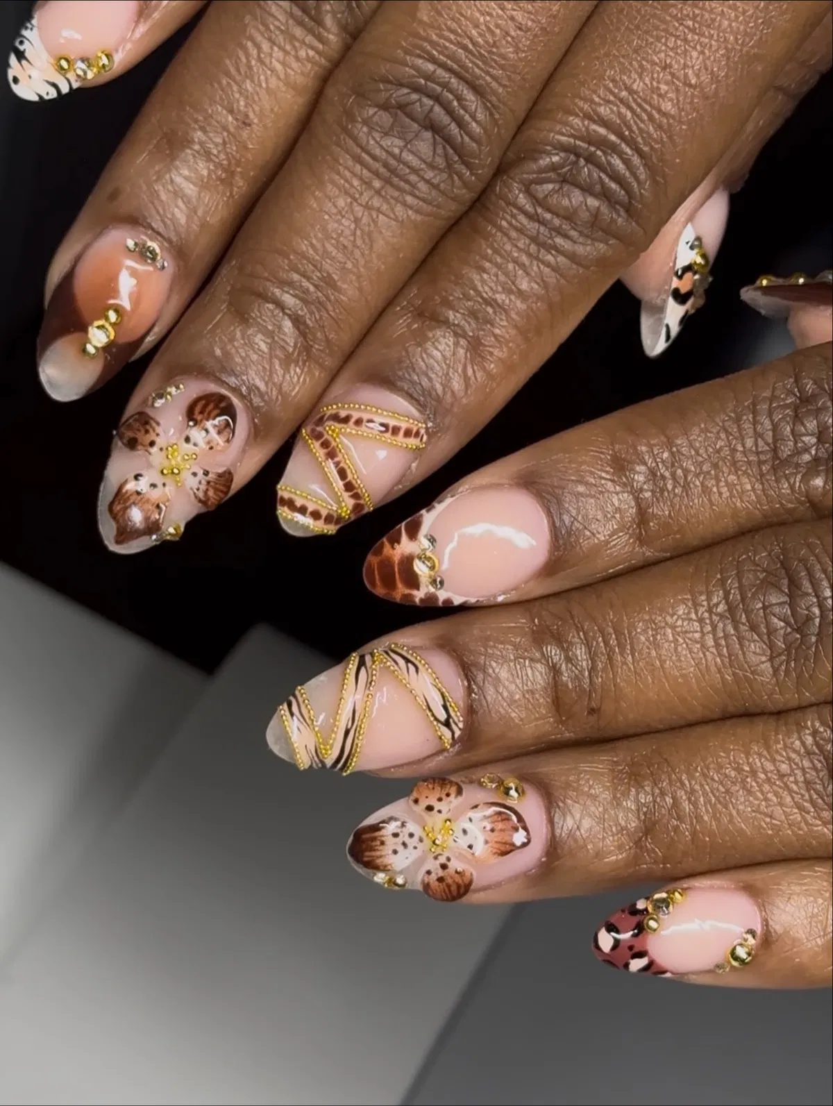 Nude-pink nails with brown spots, gold lines, and 3D floral accents