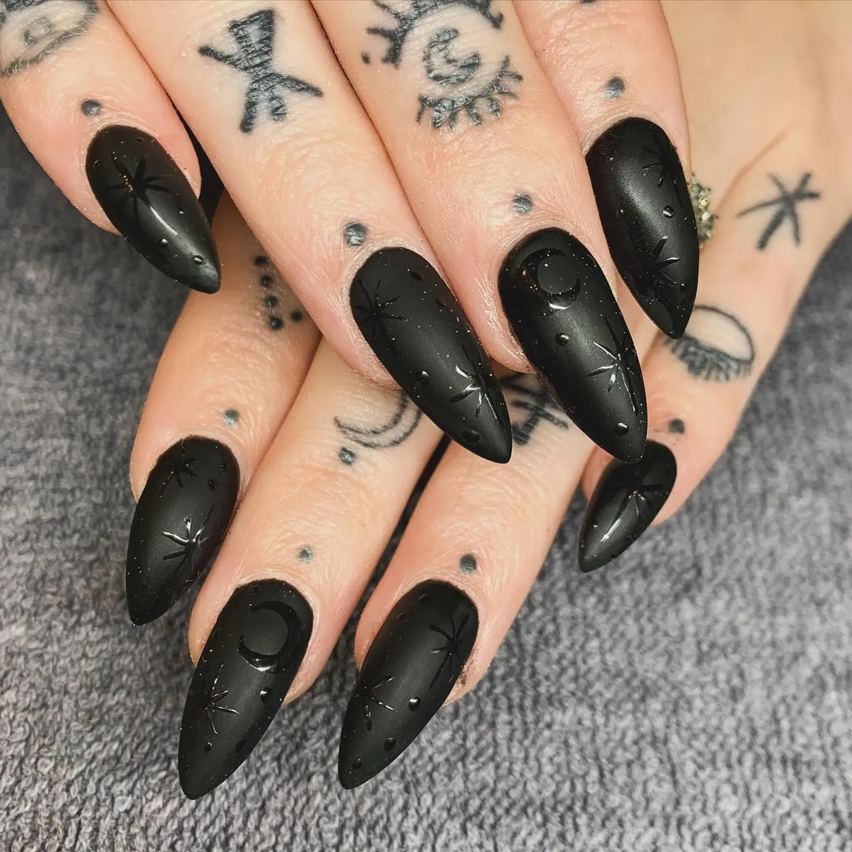 Matte black stiletto nails with textured celestial accents