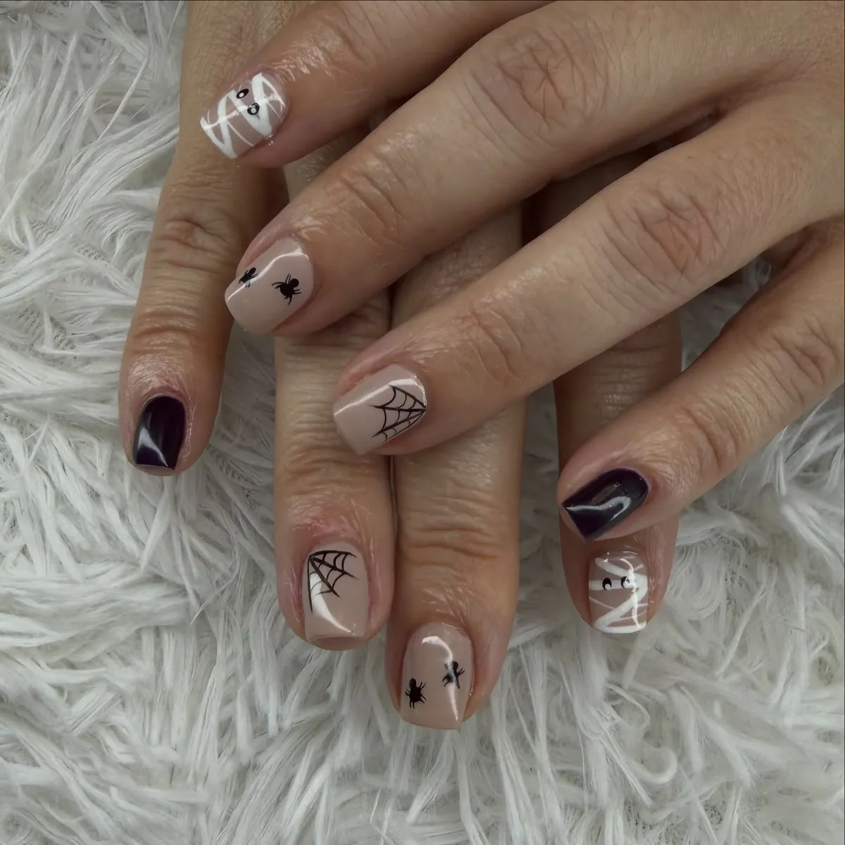 Nude and dark purple nails with webs, spiders, and bandage-style stripes