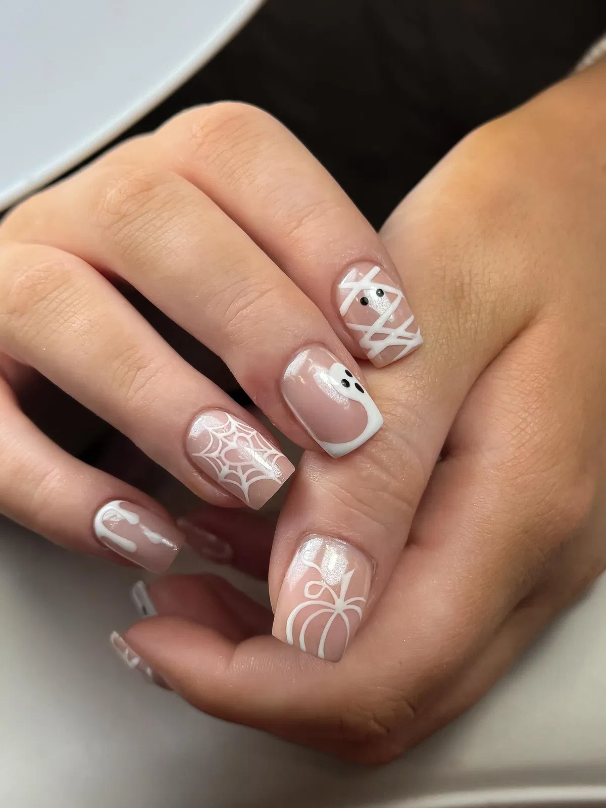 Minimal nude nails with white web, ghost, and pumpkin outlines