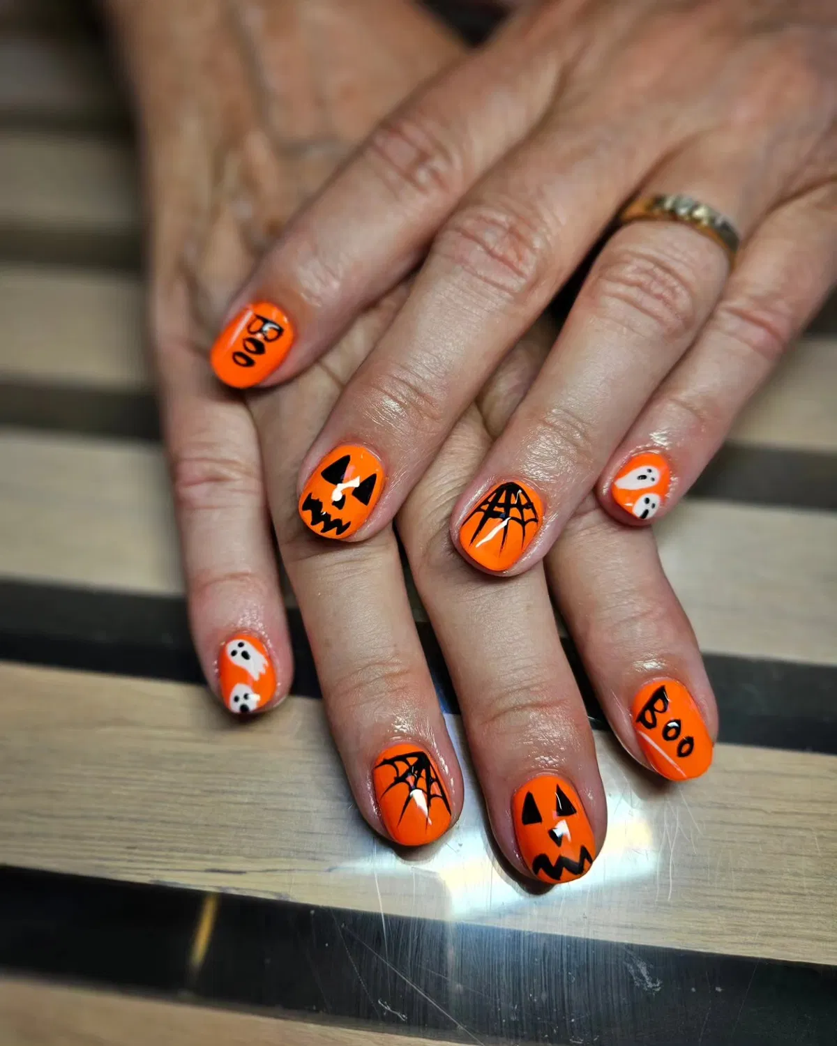 Bright orange nails with BOO text, ghosts, webs, and pumpkins
