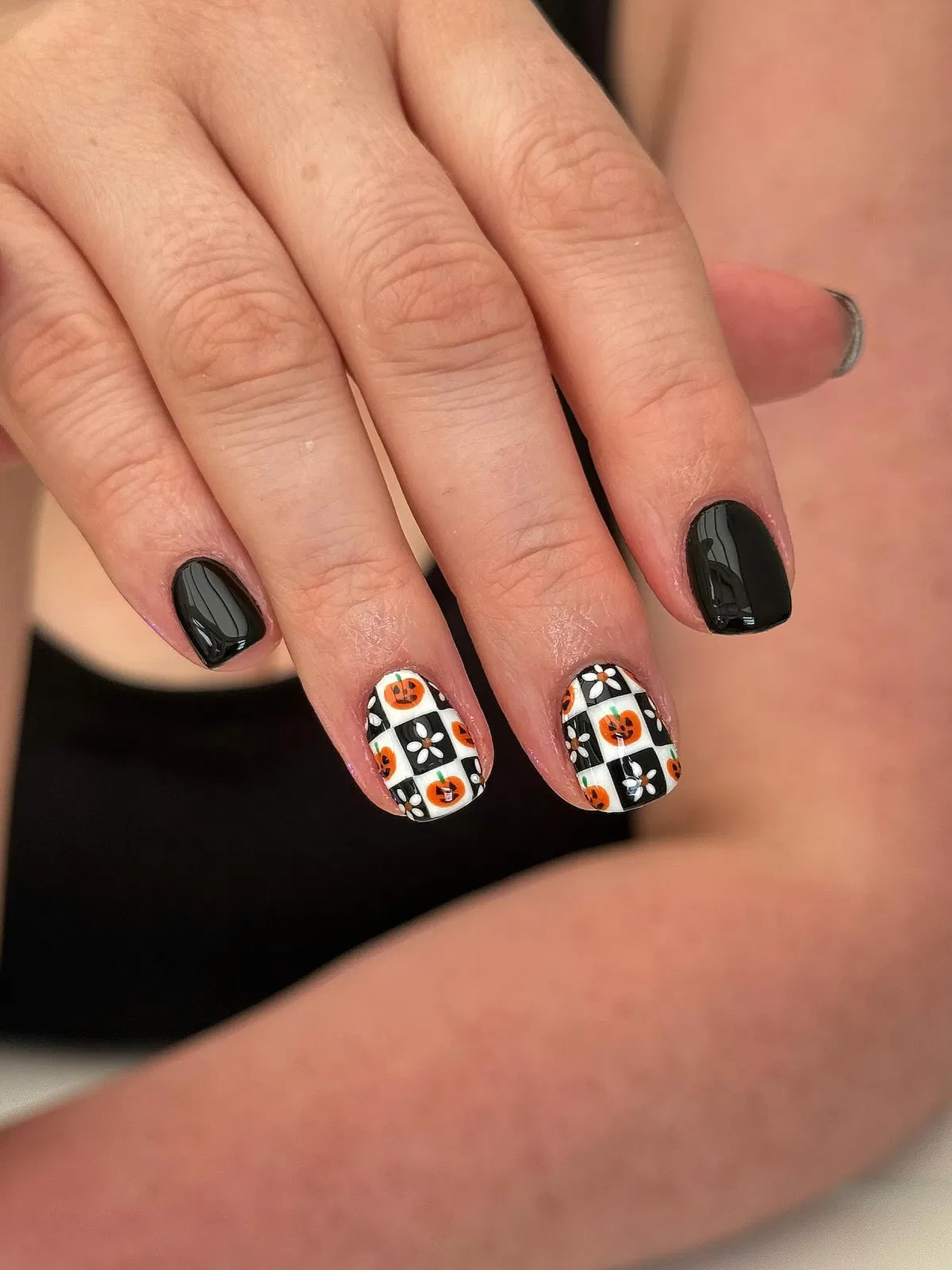 Black nails with checkerboard pumpkin-and-flower accents