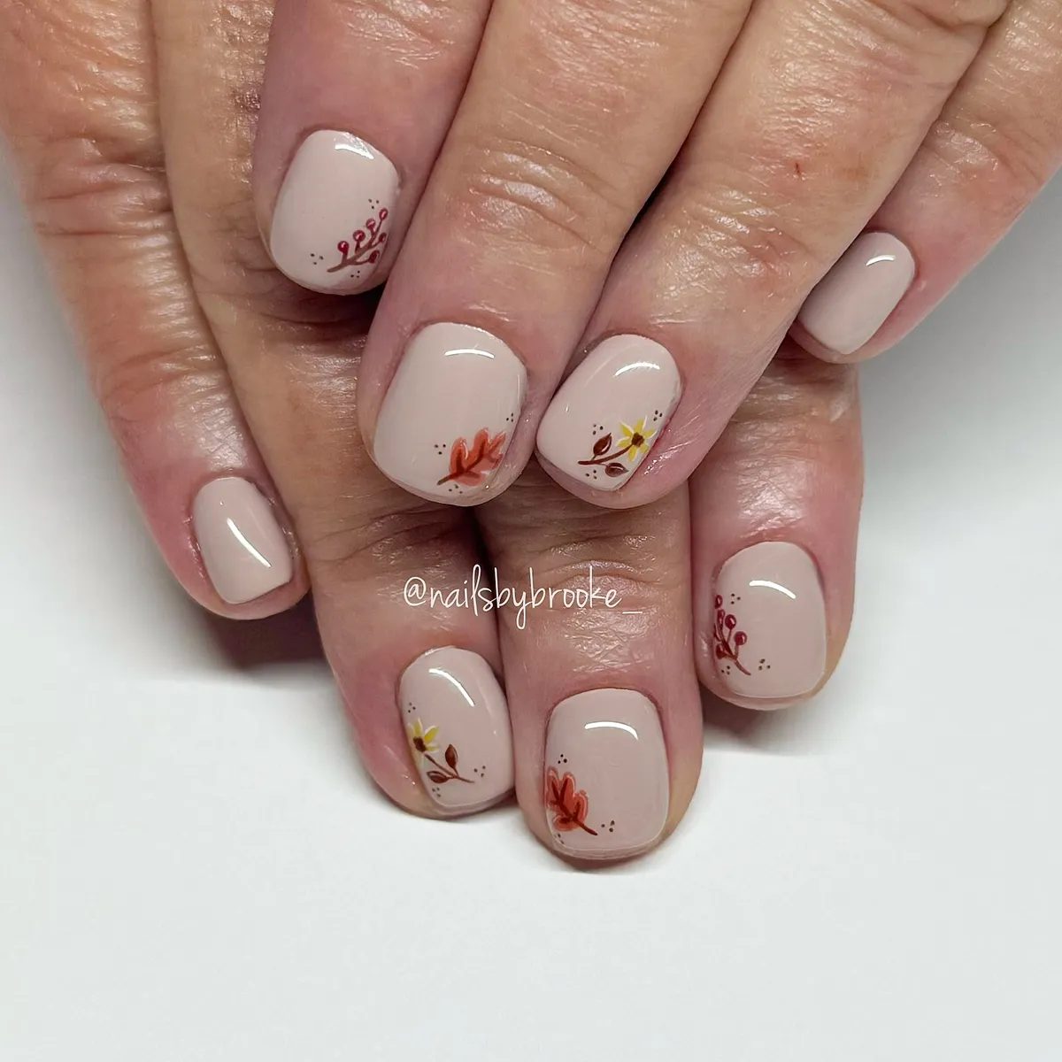 Glossy beige nails with tiny leaf accents
