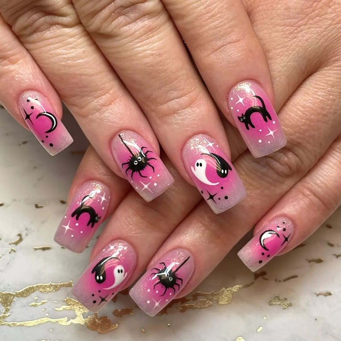 Pink gradient nails with cats, spiders, and moons
