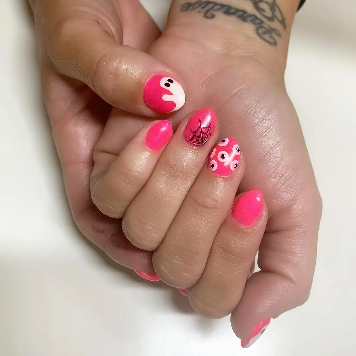 Short hot pink nails with ghost, web, and eye motifs