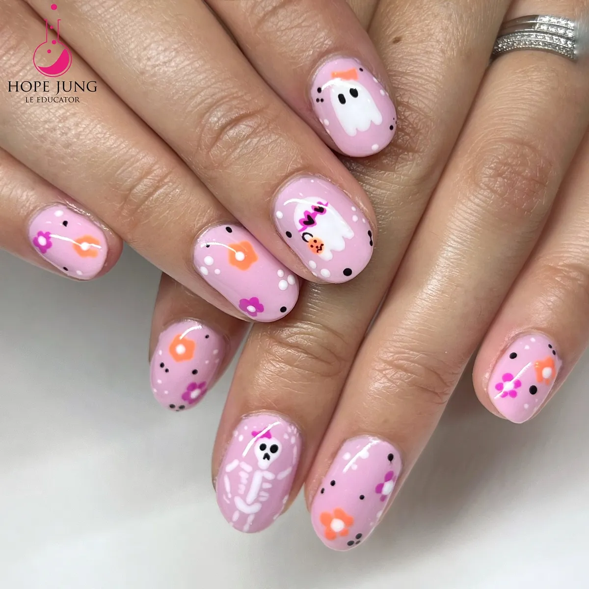 Light pink nails with dot confetti, flowers, and cute ghost/skeleton art