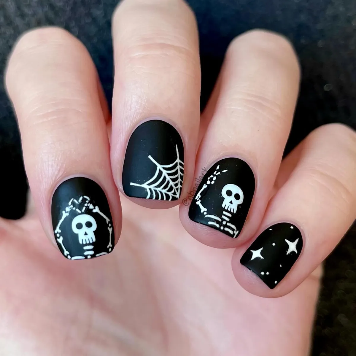 Matte black nails with white skeleton, web, and star details