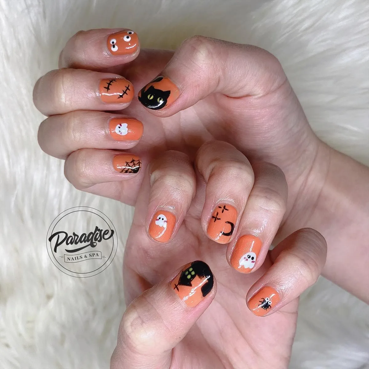 Glossy orange nails with ghosts, cat face, web, and spider details