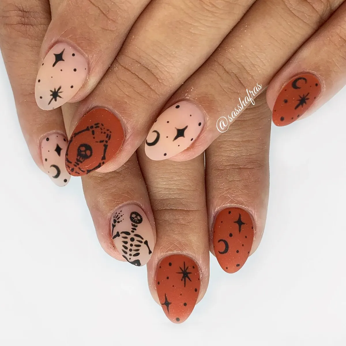 Nude and rust nails with black stars, moons, and skeleton line art