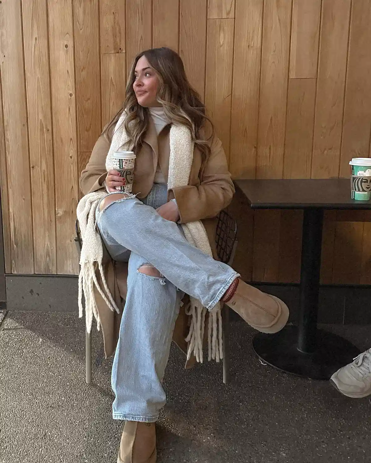 Camel coat with fringed cream scarf and ripped jeans