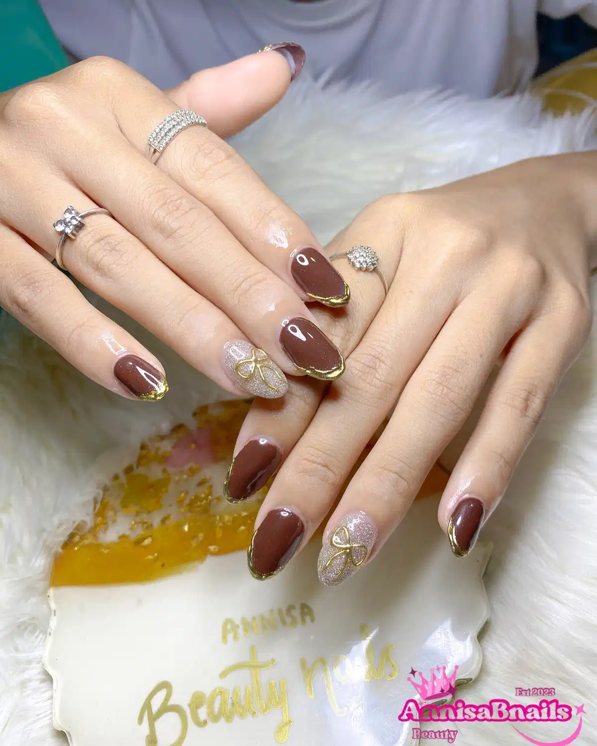 Glossy brown almonds with gold-edged tips and glitter bow accents