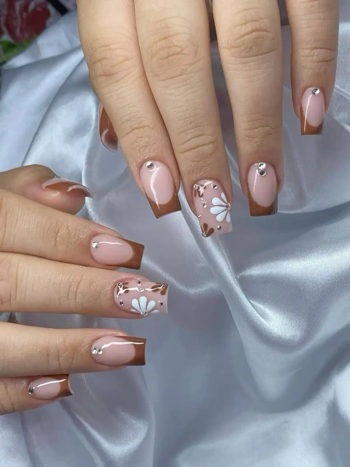 Square brown French tips with rhinestone studs and white flower accents