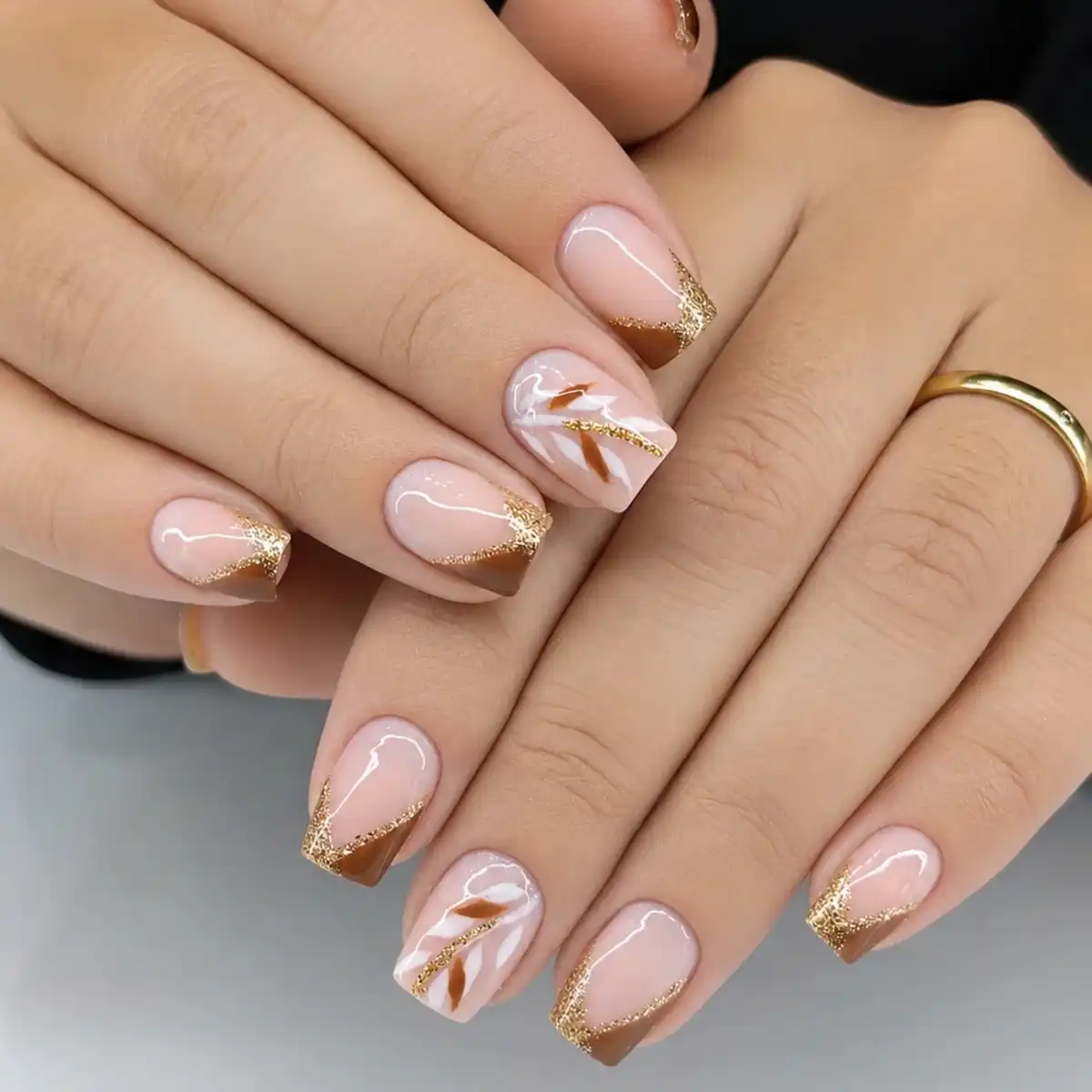 Angled brown French tips with gold glitter edging and abstract accents