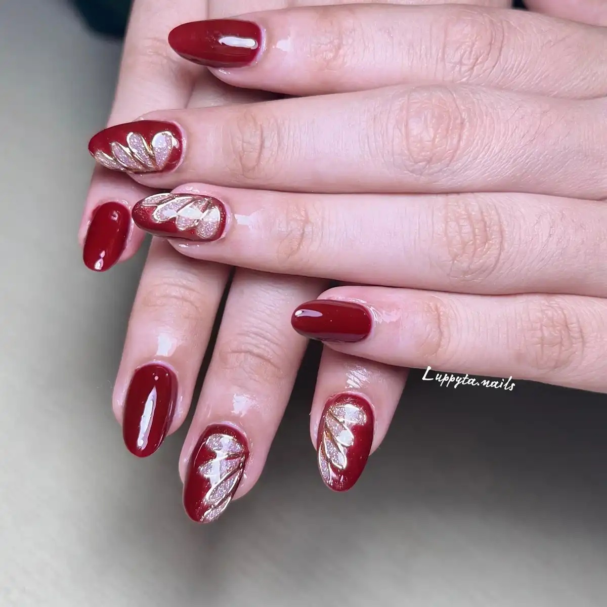 Maroon almond nails with glitter leaf-pattern accents