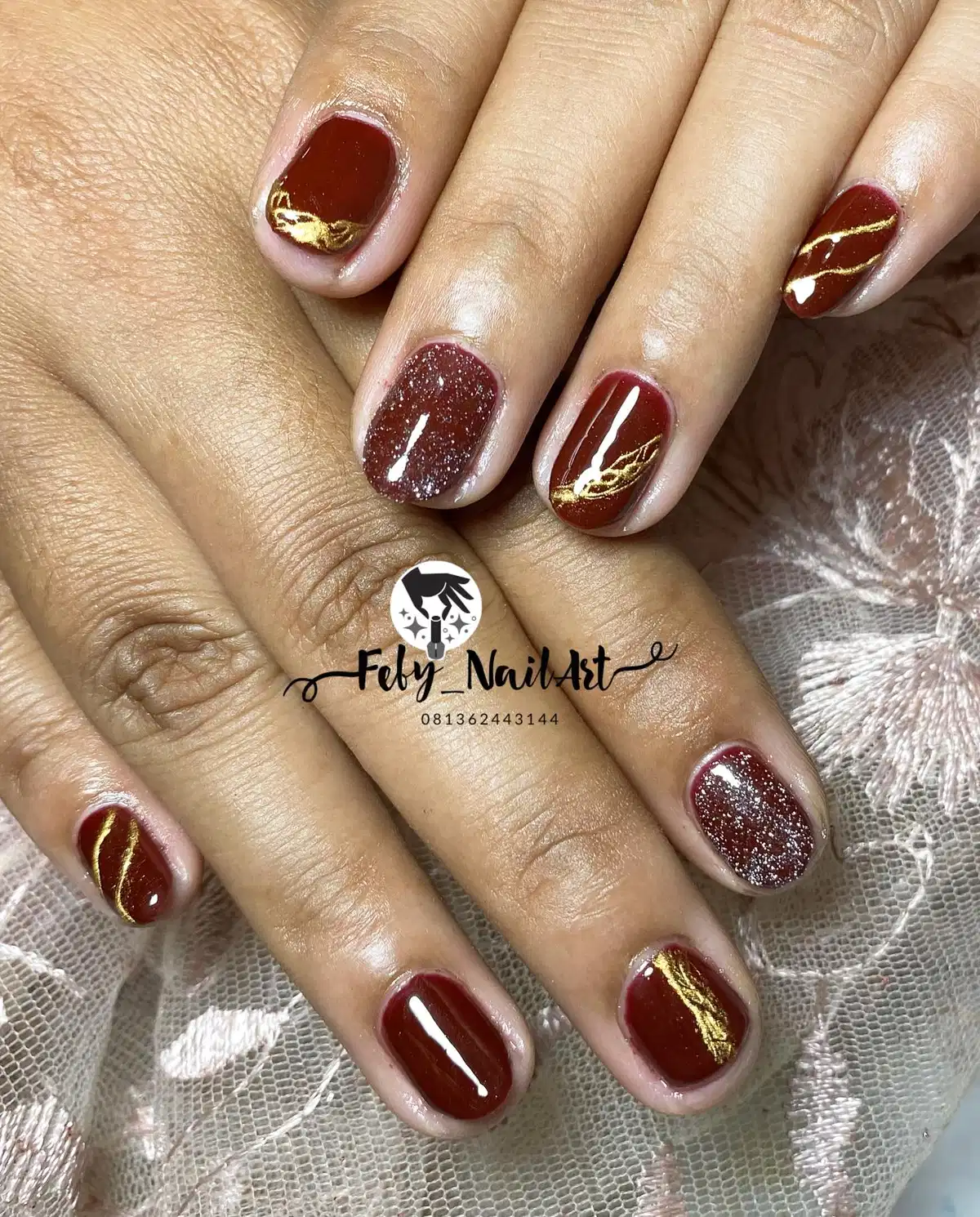 Short maroon nails with gold waves and glitter accents